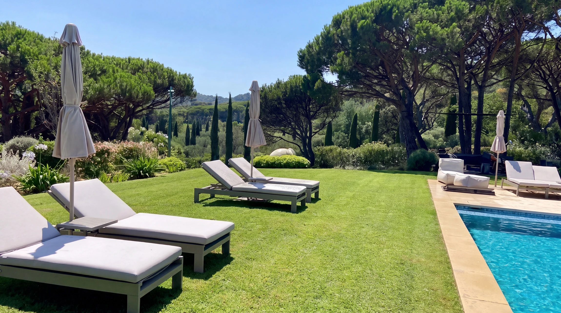 Terrasse extérieure aménagée avec salon de jardin en bois, jardin paysager en arrière-plan, bordures végétalisées et pots de fleurs colorées